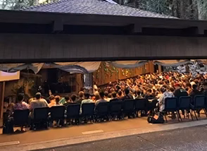 GuestRetreats-feature-meeting-spaces Outdoor dining event with many people seated at long rows of tables under a covered pavilion on a street festival scene.