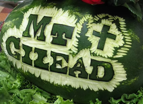 Watermelon carved with bold letters spelling 'MT GLEAD' and decorative leaf borders around the text.