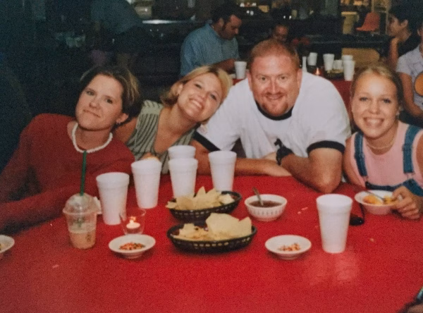 Alumni Pictures 17 Four people smiling at a table with chips, salsa, and drinks. They are sitting closely together and appear to be enjoying a meal at a casual restaurant.